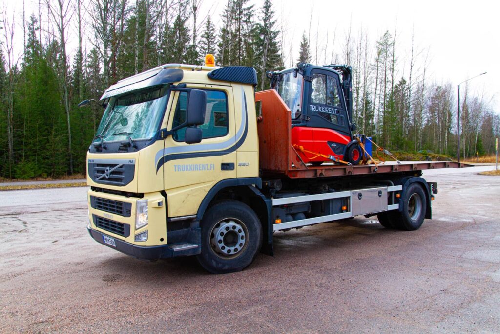 Picture of a truck from Uudenmaan Konepalvelu with a forklift loaded on board.